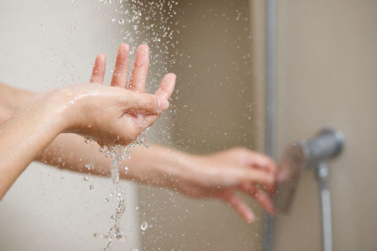 Haende unter Duschwasser vor moderner Duschrueckwand – Detailaufnahme aus dem Bad